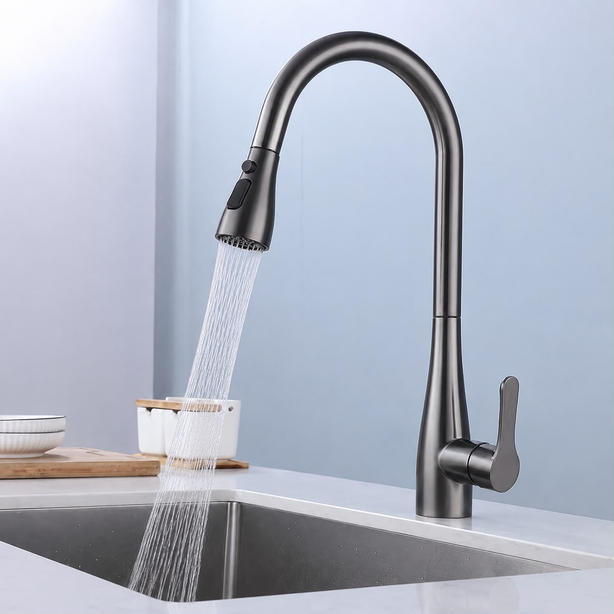 A modern dark gunmetal pull-down kitchen faucet with water running from the spray head into a stainless steel sink, shown in a clean kitchen setting.